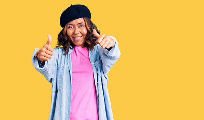 Young beautiful mixed race woman wearing french look with beret approving doing positive gesture with hand, thumbs up smiling and happy for success. winner gesture.