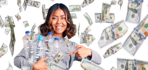 Young beautiful mixed race woman holding recycling plastic bottles smiling happy pointing with hand and finger