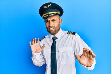 Handsome man with beard wearing airplane pilot uniform disgusted expression, displeased and fearful...