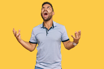 Handsome man with beard wearing casual clothes crazy and mad shouting and yelling with aggressive expression and arms raised. frustration concept.