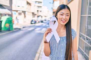 Young chinese woman smiling happy holding white ribbon at street of city.