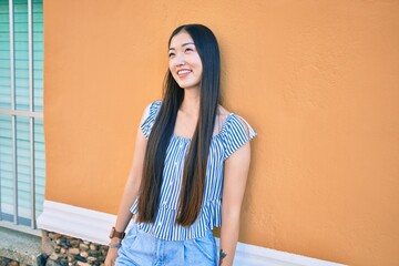 Fototapeta premium Young chinese woman smiling happy leaning on the wall at street of city.