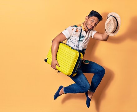 Young handsome latin man on vacation wearing summer clothes smiling happy. Jumping with smile on face holding cabin bag over isolated background