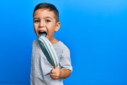 Adorable latin toddler eating delicious lollipop over isolated blue background.