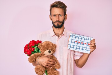 Handsome caucasian man with beard holding bear and bouquet of flowers for anniversary skeptic and...