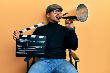 Handsome man with tattoos holding video film clapboard and louder angry and mad screaming...