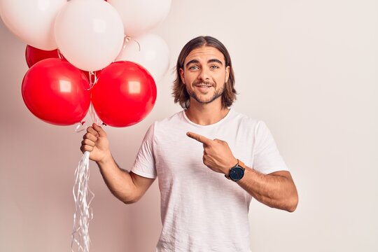 Young handsome man holding balloons smiling happy pointing with hand and finger