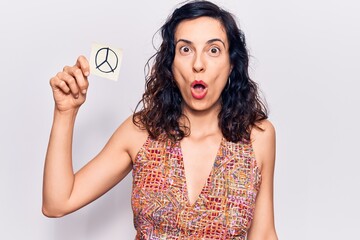 Young beautiful hispanic woman holding peace symbol reminder paper scared and amazed with open mouth for surprise, disbelief face