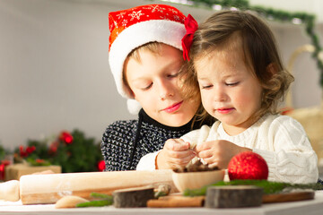 Little cute girl 2-4 with a red bow and boy 7-10 in a Christmas cap make gingerbread cookies in the New Year's kitchen.