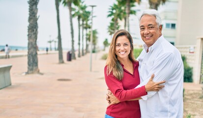 Obraz premium Middle age hispanic couple smiling happy and hugging walking at street.