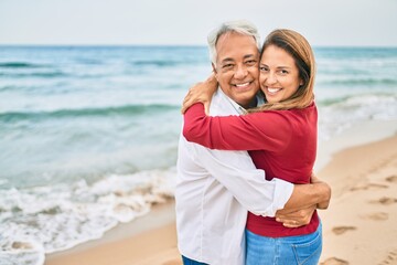 Fototapeta na wymiar Middle age hispanic couple smiling happy and hugging walking at the beach