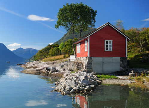 Red Wooden Boat House On The Shore Of The Lustrafjord In Hoyheimsvik On A Sunny Summer Day With A Clear Blue Sky And A Few Clouds