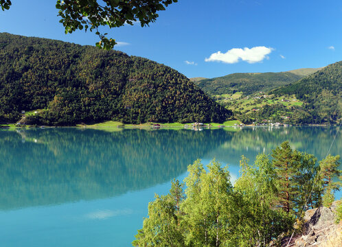 Mountains Reflecting In The Beautiful Turquoise Water Of The Lustrafjord On A Sunny Summer Day With A Clear Blue Sky And A Few Clouds
