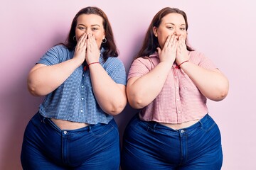 Young plus size twins wearing casual clothes laughing and embarrassed giggle covering mouth with...