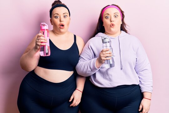 Young plus size twins wearing sportswear drinking bottle of water scared and amazed with open mouth for surprise, disbelief face