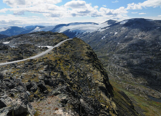 Fototapeta na wymiar Winding Road From Dalsnibba Into The Barren Valley Surrounded By Glacier Covered Mountains To Geirangerfjord On A Sunny Summer Day With A Clear Blue Sky And A Few Clouds