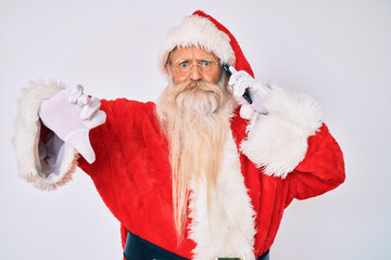 Old senior man wearing santa claus costume speaking on the phone with angry face, negative sign showing dislike with thumbs down, rejection concept