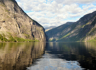 Fototapeta premium Mountains Reflecting In The Calm Water Of Geirangerfjord On A Sunny Summer Day With A Clear Blue Sky And A Few Clouds