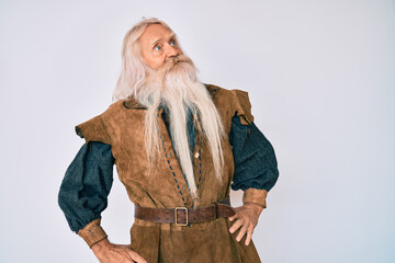 Old senior man with grey hair and long beard wearing viking traditional costume smiling looking to the side and staring away thinking.