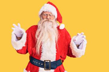Old senior man with grey hair and long beard wearing traditional santa claus costume smiling funny doing claw gesture as cat, aggressive and sexy expression