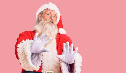 Old senior man with grey hair and long beard wearing traditional santa claus costume moving away hands palms showing refusal and denial with afraid and disgusting expression. stop and forbidden.