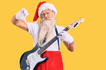 Old senior man with grey hair and long beard wearing santa claus costume playing electric guitar with angry face, negative sign showing dislike with thumbs down, rejection concept