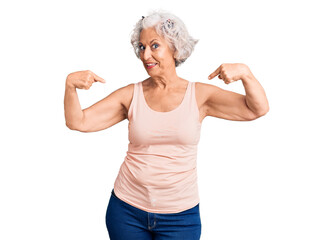 Senior grey-haired woman wearing casual clothes looking confident with smile on face, pointing...