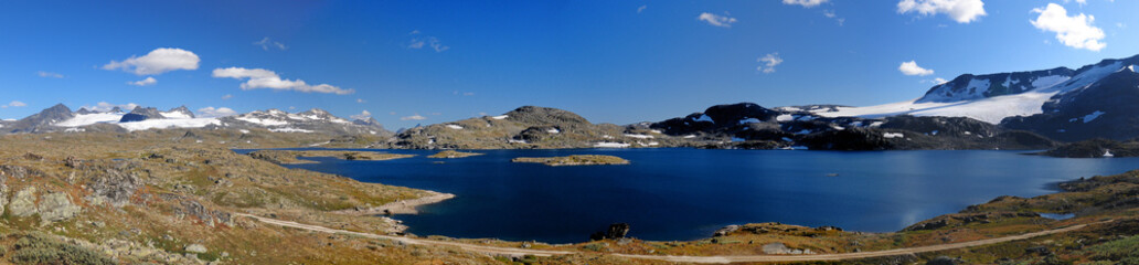 Panorama View Of Lakes And Glaciers In The Barren Landscape Of The Icefields Of Jotunheimen National Park On A Sunny Summer Day With A Clear Blue Sky And A Few Clouds