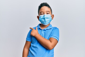 Little boy hispanic kid wearing medical mask smiling cheerful pointing with hand and finger up to the side
