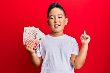 Little boy hispanic kid holding 20 israel shekels banknotes smiling happy pointing with hand and...