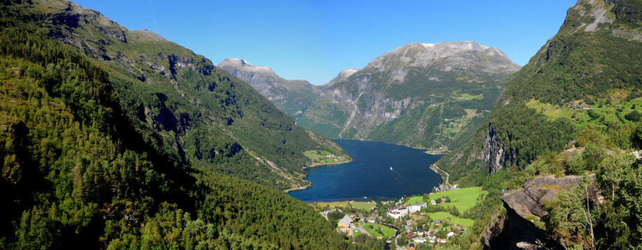 Panorama View From Flydalsjuvet Lookout To Geiranger Village And Geirangerfjord On A Sunny Summer Day With A Clear Blue Sky