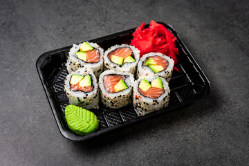 Delivery of Japanese traditional food. Salmon and avocado rolls with black and white sesame seeds in a plastic container