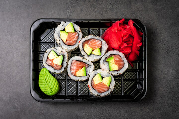 Delivery of Japanese traditional food. Salmon and avocado rolls with black and white sesame seeds in a plastic container. Top view