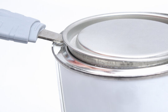 A Man Opens A Jar Of White Paint With A Can Opener On A White Background. Renovation Concept.