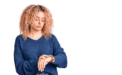Young blonde woman with curly hair wearing casual winter sweater checking the time on wrist watch,...