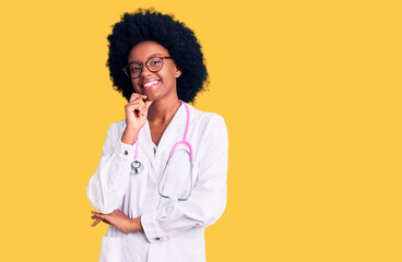 Young african american woman wearing doctor coat and stethoscope looking confident at the camera smiling with crossed arms and hand raised on chin. thinking positive.