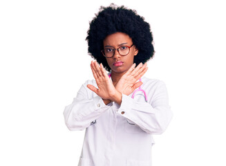 Young african american woman wearing doctor coat and stethoscope rejection expression crossing arms doing negative sign, angry face