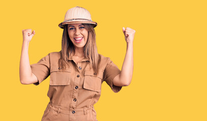 Young beautiful woman wearing explorer hat screaming proud, celebrating victory and success very excited with raised arms