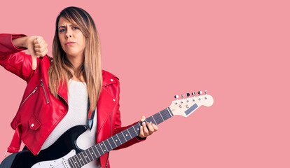 Fototapeta premium Young beautiful woman playing electric guitar with angry face, negative sign showing dislike with thumbs down, rejection concept