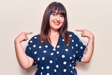Young plus size woman wearing casual clothes looking confident with smile on face, pointing oneself...