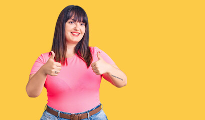 Young plus size woman wearing casual clothes success sign doing positive gesture with hand, thumbs up smiling and happy. cheerful expression and winner gesture.