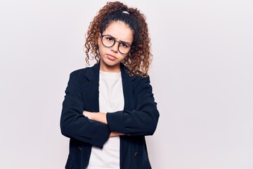 Beautiful kid girl with curly hair wearing business clothes and glasses skeptic and nervous, disapproving expression on face with crossed arms. negative person.