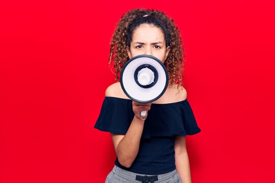Adorable latin teenager girl with angry expression. Screaming loud using megaphone standing over isolated red background