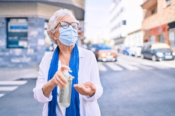 Elder senior woman with grey hair wearing coronavirus safety mask and using sanitizer gel outdoors