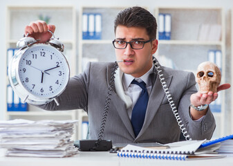 Businessman smoking holding human skull and an alarm clock in th