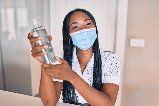 Young african american woman wearing medical mask using sanitizer hand gel at home