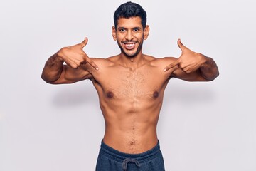 Young latin man standing shirtless looking confident with smile on face, pointing oneself with...