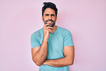 Obraz premium Handsome hispanic man with beard wearing casual clothes looking confident at the camera with smile with crossed arms and hand raised on chin. thinking positive.