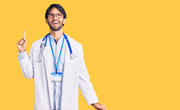 Handsome hispanic man wearing doctor uniform and stethoscope pointing finger up with successful idea. exited and happy. number one.