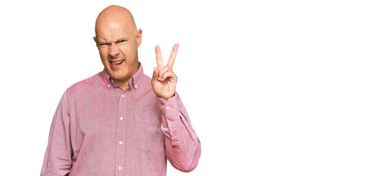 Middle age bald man wearing casual clothes smiling with happy face winking at the camera doing victory sign. number two.